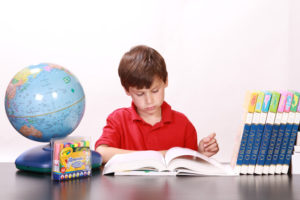 little boy reading a book with classroom supplies