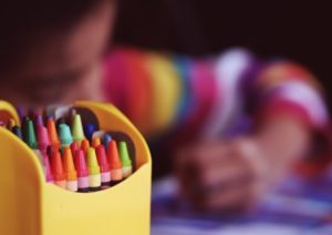 box of crayons in front of blurred child coloring 