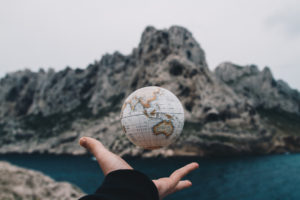 small globe hovering above a hand with a mountain and water backdrop