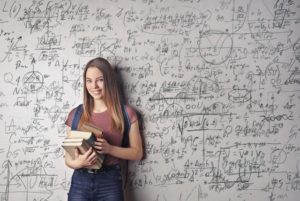 teen student holding books and standing in front of whiteboard full of equations 