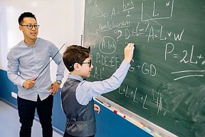 boy writing equation on chalkboard with teacher watching
